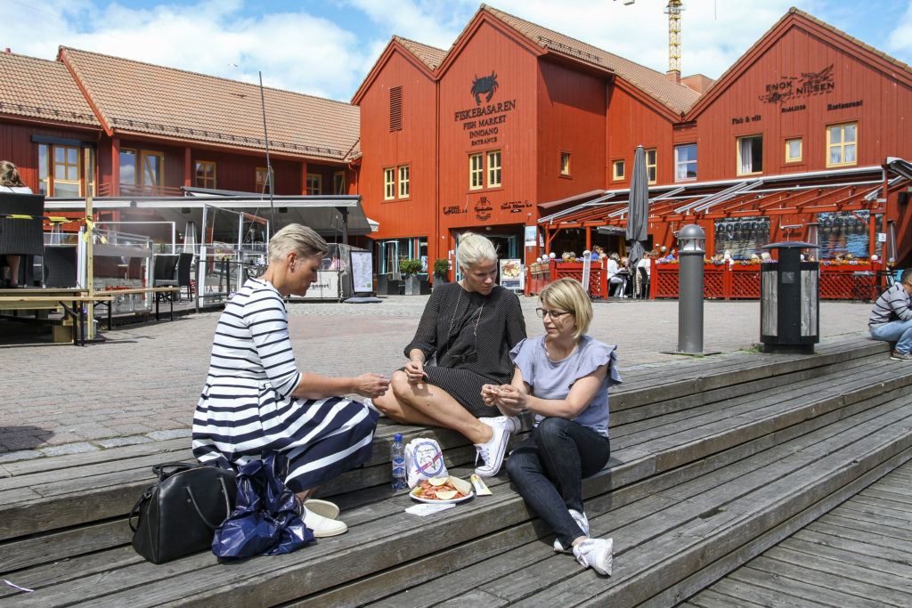 Drei Frauen sitzen vor dem Fischmarkt in Kristiansand und pulen Shrimps